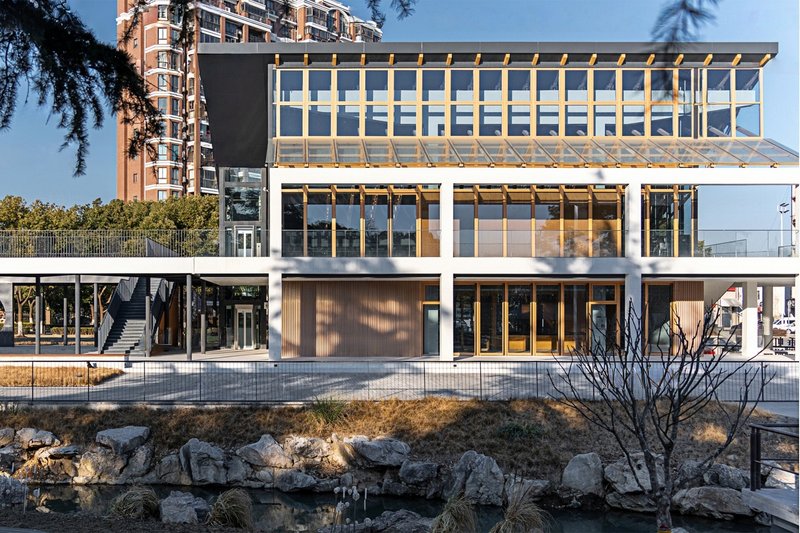 Waterside facade showing the timber-framed glass pavilion atop a concrete podium with planted rockery below