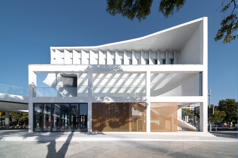Street elevation showing layered white volumes with recessed timber screens and deep shadow patterns in afternoon light