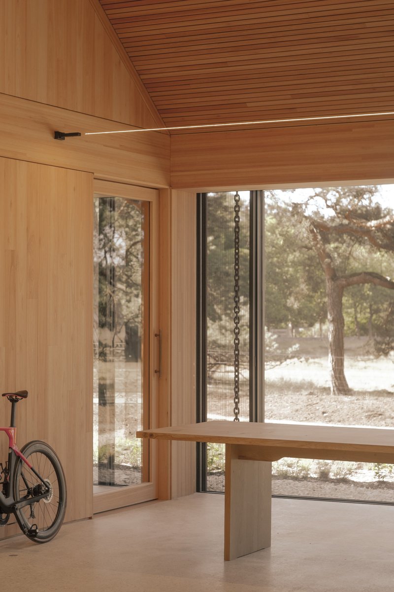 Interior workspace with suspended timber table, glass door, and wide window overlooking trees