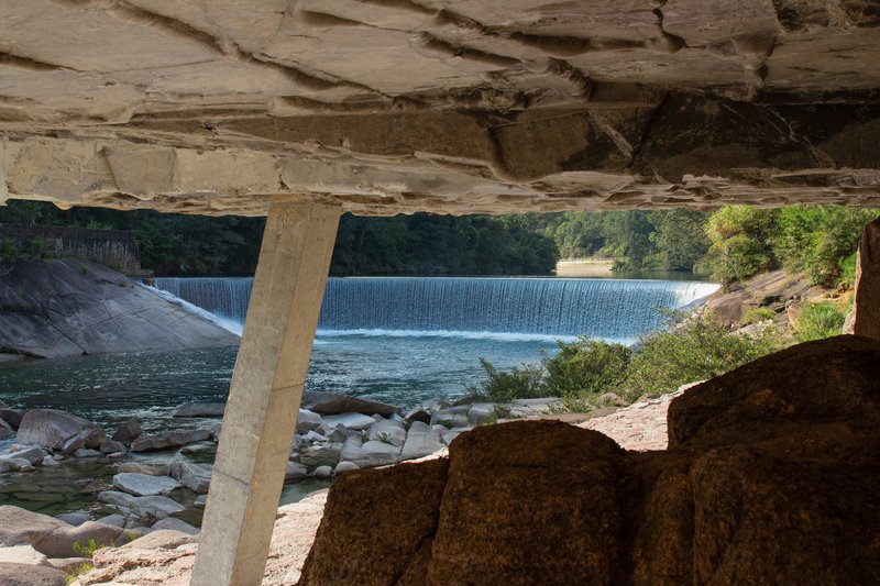 View from beneath the roof overhang framing the cascading weir and river through concrete columns