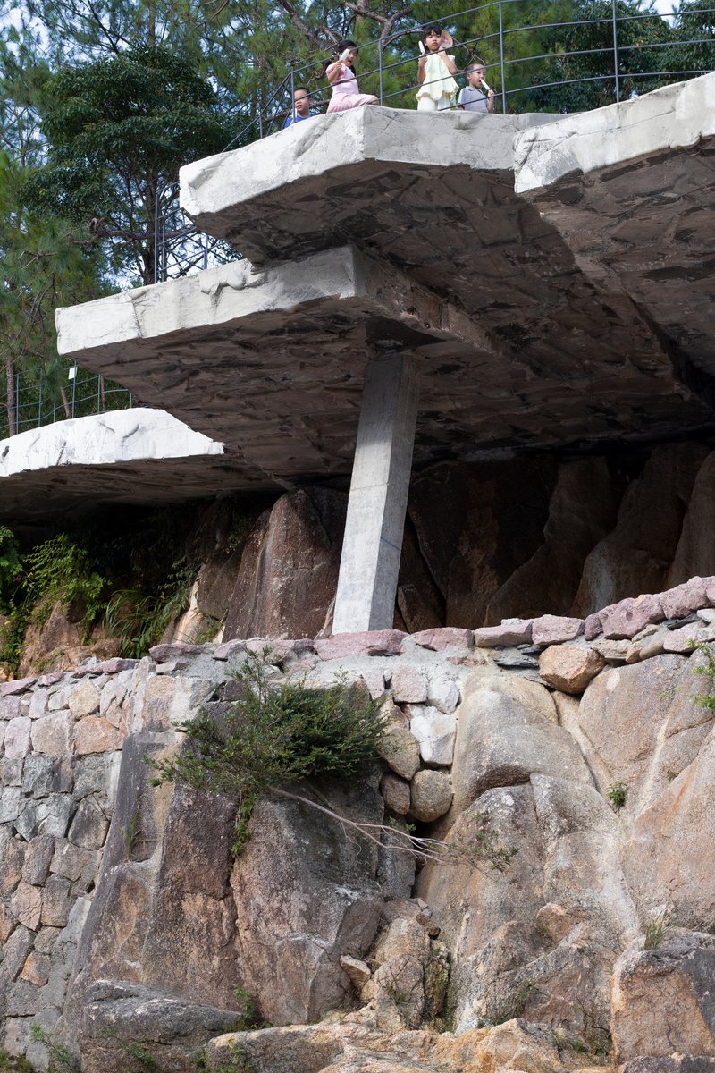 Angled view of cantilevered concrete platforms on stone pillar with visitors above and boulders below