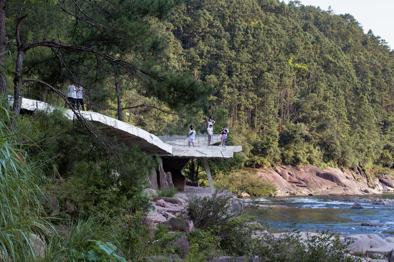 Cantilevered concrete observation deck extending over a river with visitors and forested hillside beyond