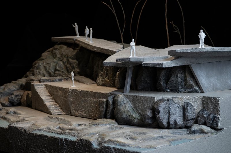 Side view of the model revealing multiple cantilevered levels with figures standing on terraced platforms