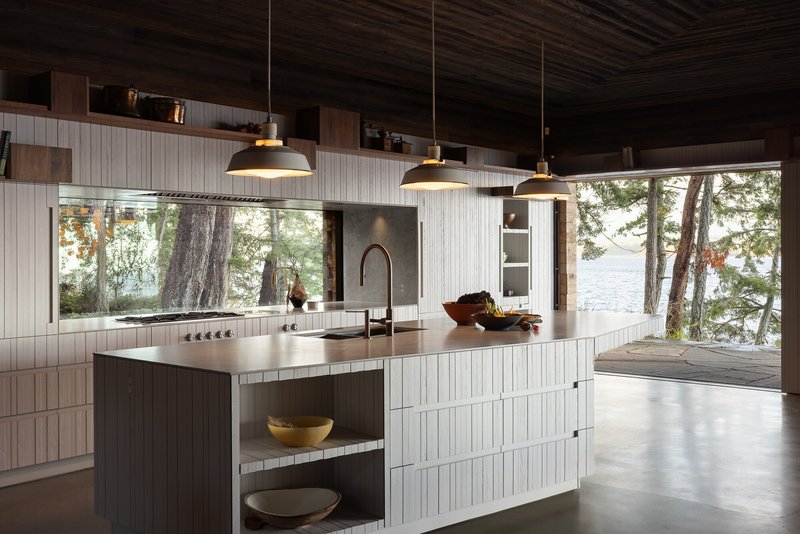 Kitchen island with pale vertical-board cabinetry and wide window overlooking lakeside trees