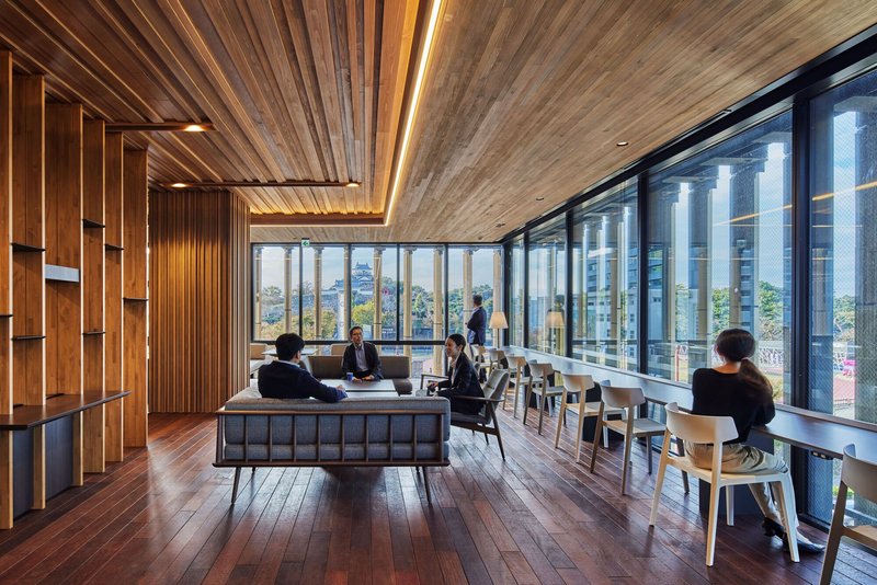 Upper floor lounge with timber ceiling, floor-to-ceiling glazing, and occupied seating areas overlooking the surroundings