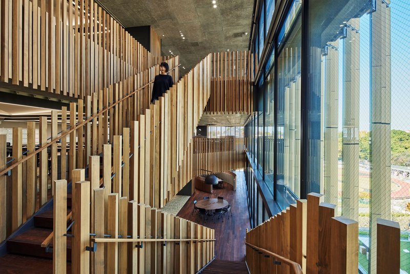 Interior view through vertical timber battens toward the glazed facade with figures on stairs and seating