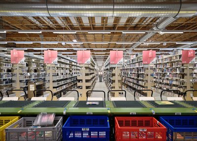 This image shows the interior of a large warehouse or library, featuring rows of shelves filled with