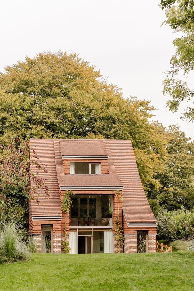Red clay tile facade with folded roof planes rising from a mowed lawn surrounded by trees