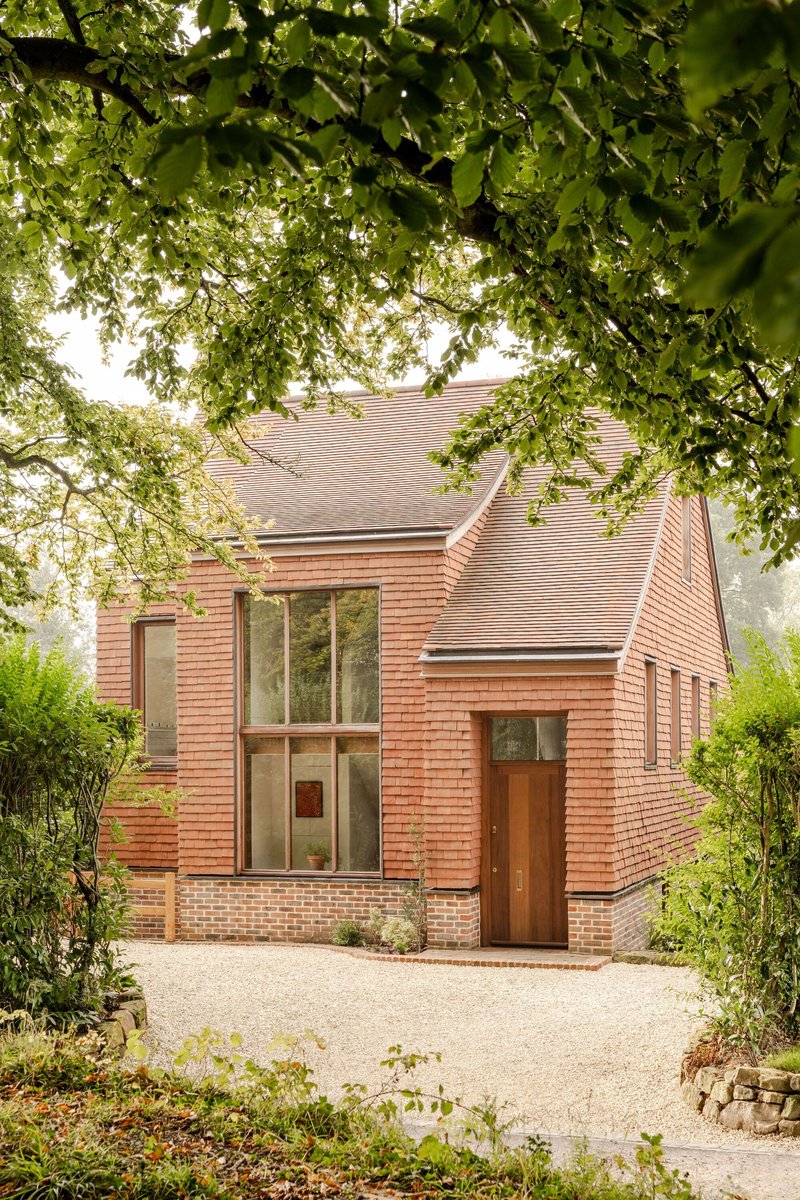 Street view of the terracotta tile facade and timber entry door framed by overhanging tree branches