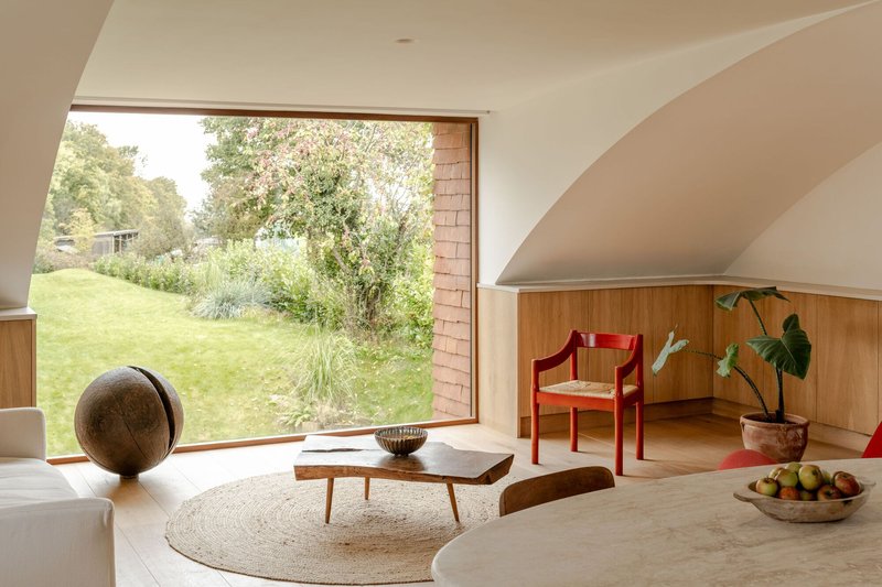 Living space with large picture window overlooking garden and curved ceiling above timber paneling