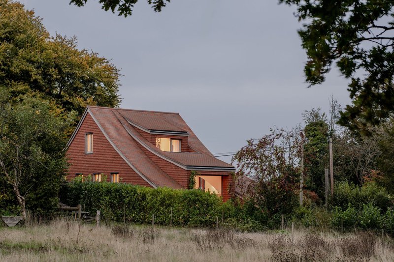 The sculptural roof silhouette illuminated at dusk behind a hedge and wild grassland
