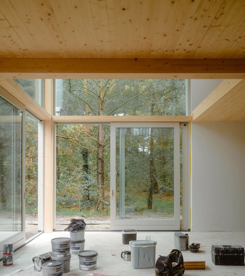 Interior view through large timber-framed windows overlooking trees in autumn with paint buckets on the floor