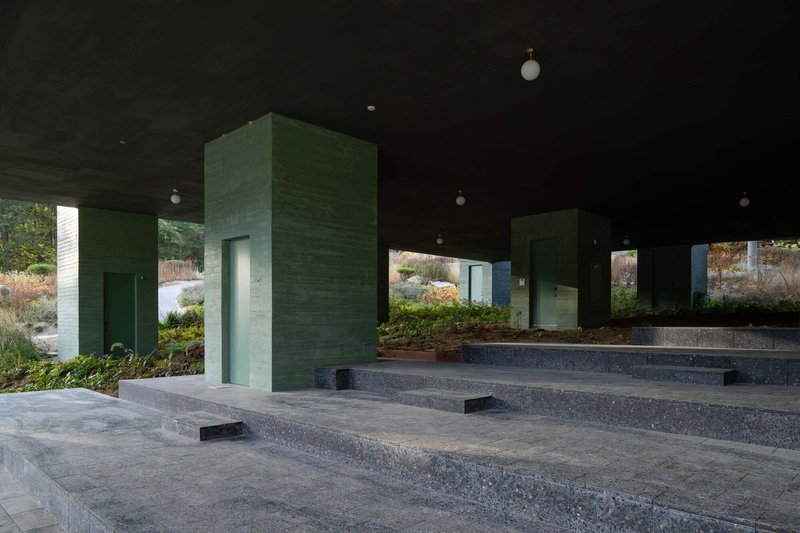 Stepped terrazzo platforms with green concrete service towers beneath the elevated building volume