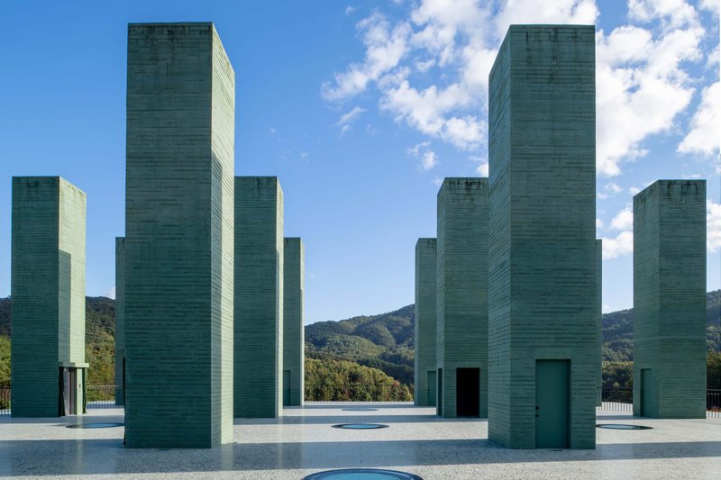 Grid of varied-height concrete towers framing distant hills under blue sky with clouds