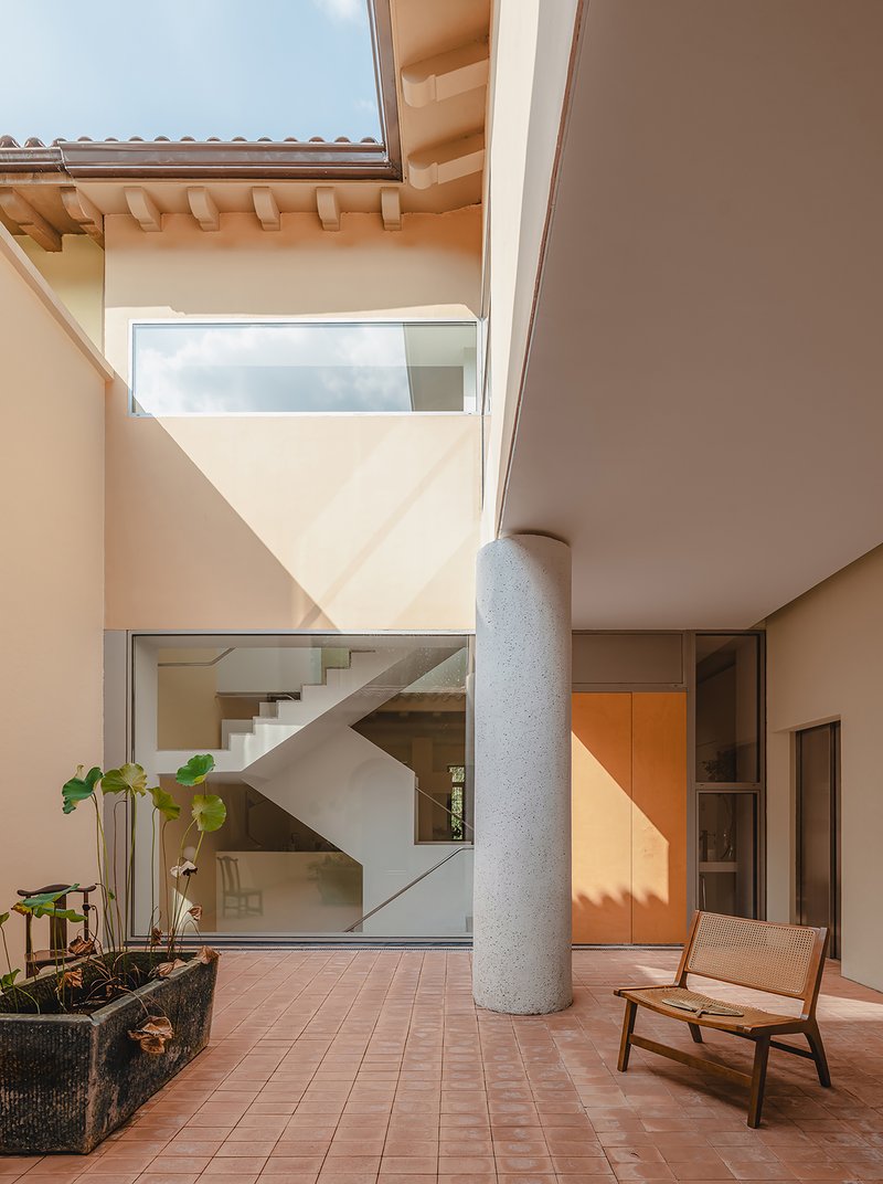 Terracotta tile courtyard with cylindrical concrete column and view to interior staircase above
