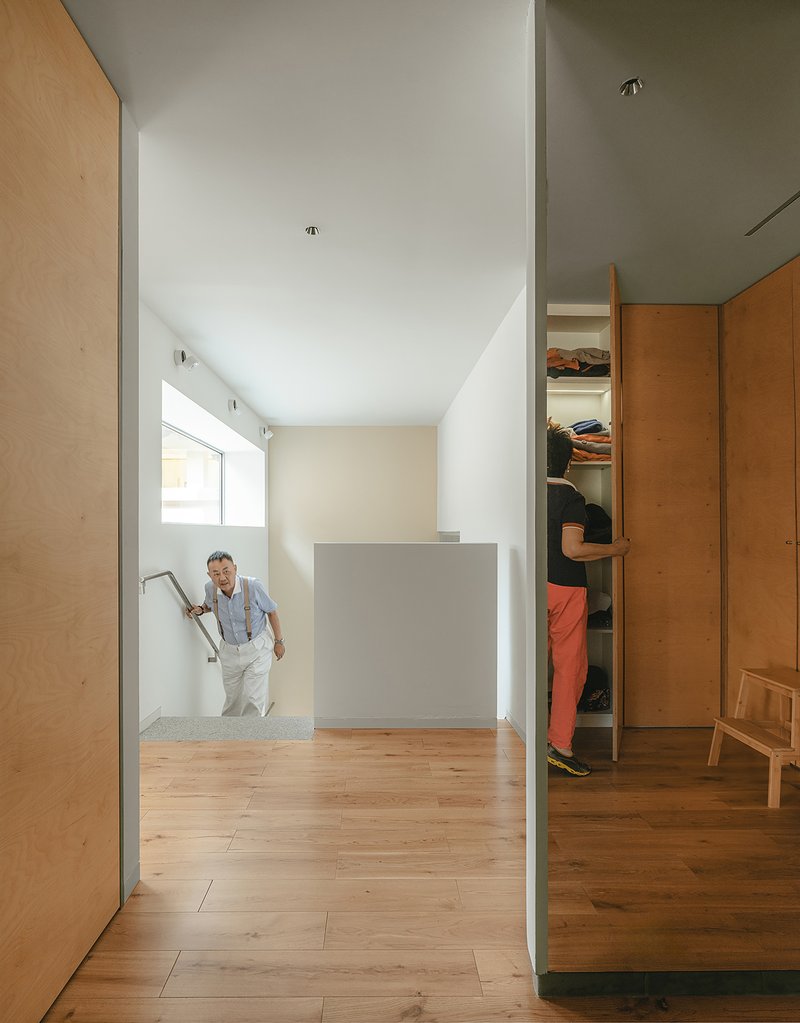 Timber-lined hallway with person descending stairs toward an open wardrobe niche