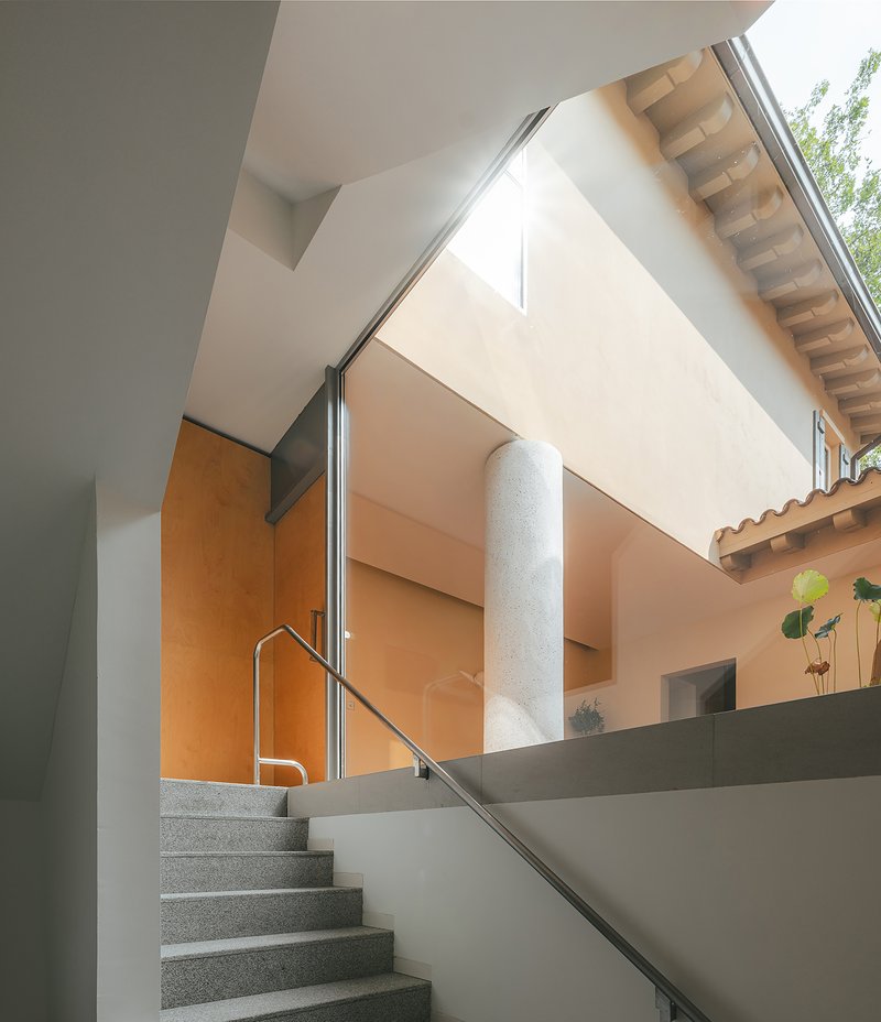 Terrazzo staircase with stainless steel handrail rising toward a light-filled upper level