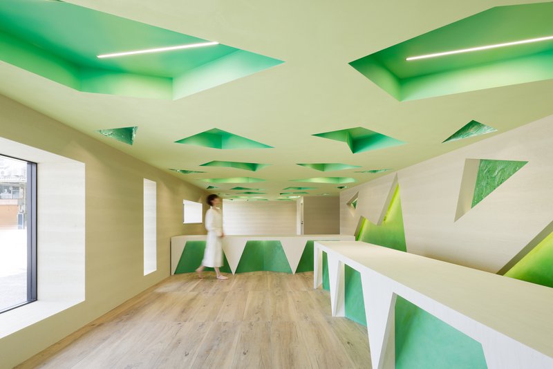Wide view of the office interior with green-painted angular ceiling cavities and triangular wall recesses