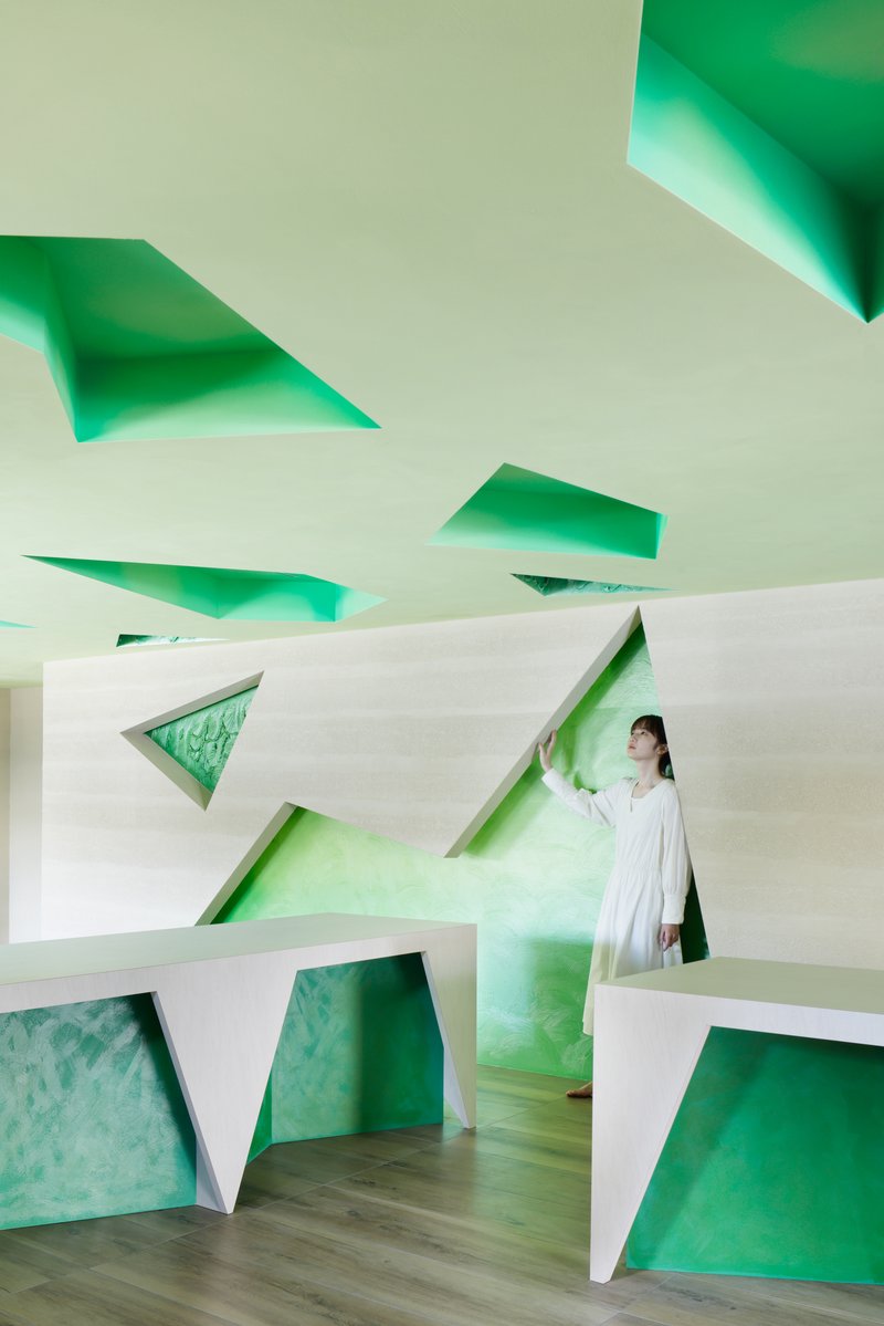 A figure leans against the wall framed by triangular openings on the wall and ceiling
