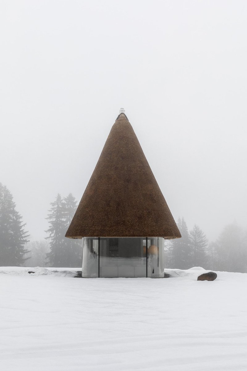 Front elevation of the conical thatched pavilion surrounded by fog and evergreen trees
