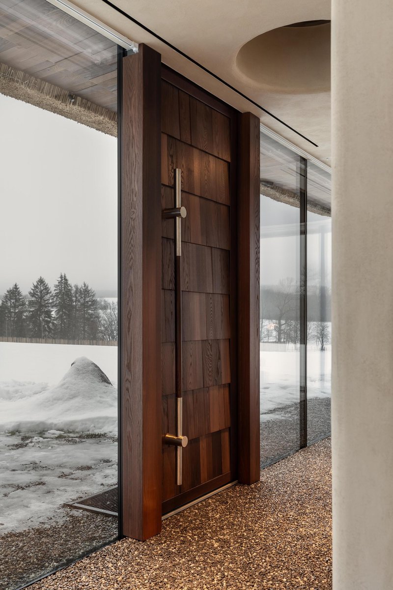 Horizontal timber-paneled entry door with bronze lever handles opening to snowy exterior