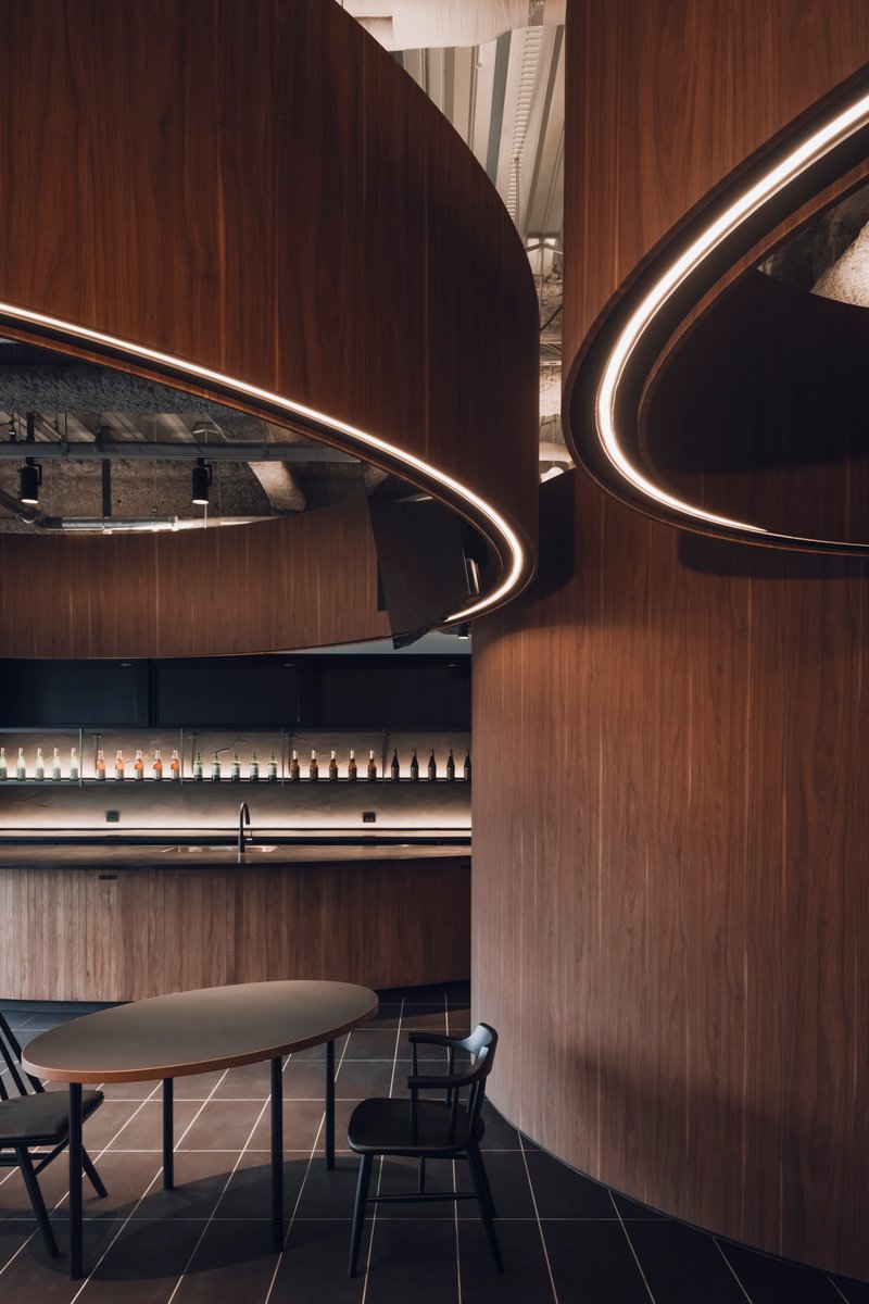 Close-up of overlapping curved timber walls with integrated LED ring lighting beneath exposed structural ceiling