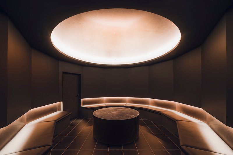 Circular room with backlit curved banquettes surrounding a central table beneath an illuminated ceiling oculus