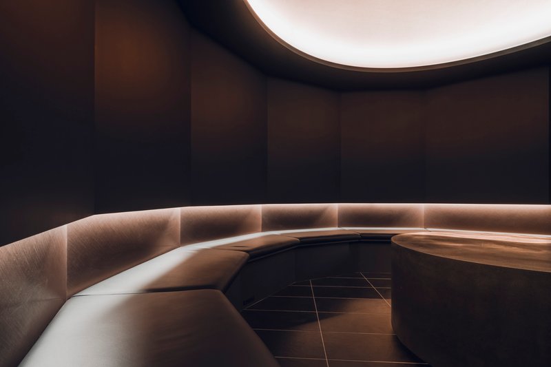 Curved bench with integrated strip lighting along its base against dark walls under a rounded ceiling