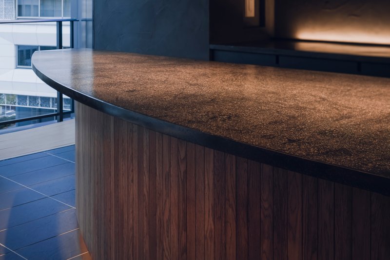 Close-up of the curved stone counter edge with walnut base cladding near a glazed opening