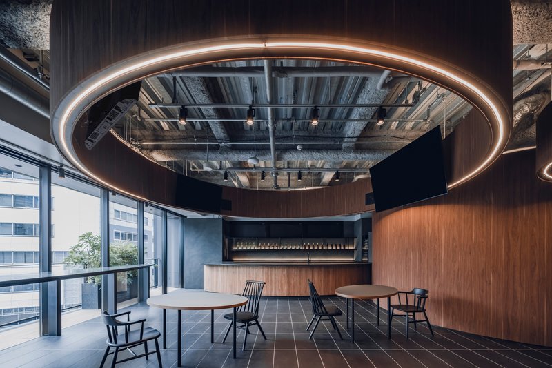 Breakroom with circular walnut-clad volumes and ring lighting suspended below exposed mechanical ceiling