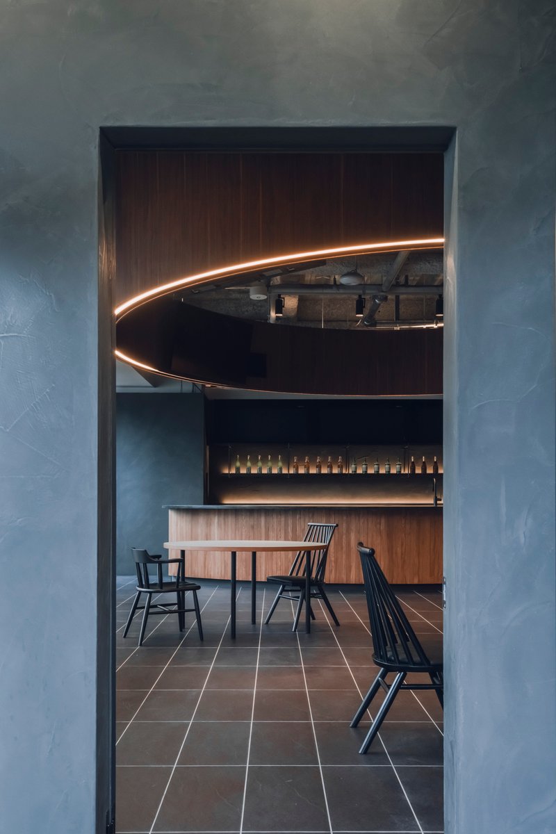 View through doorway framed by textured grey walls toward dining space with curved illuminated canopy overhead