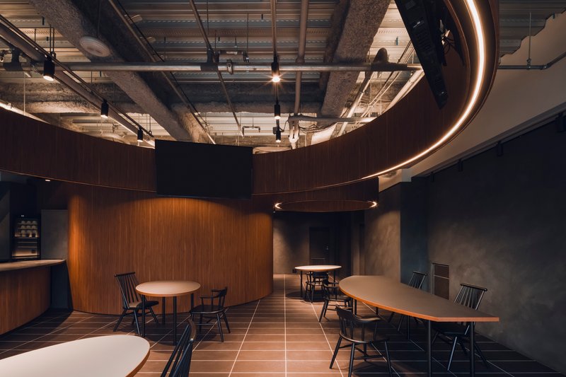 Open dining area with curved walnut volumes, dark grey tile flooring, and illuminated circular ring pendant