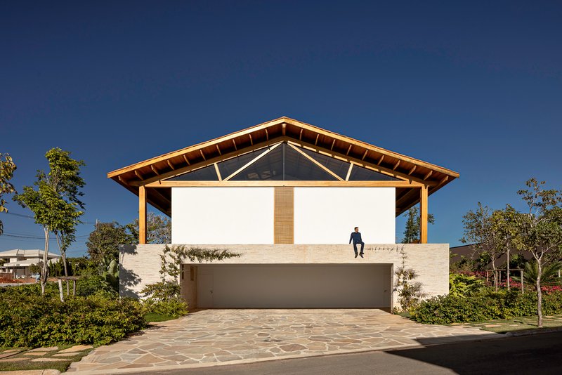 Street facade with exposed timber roof structure, white masonry base, and a figure standing on the upper terrace