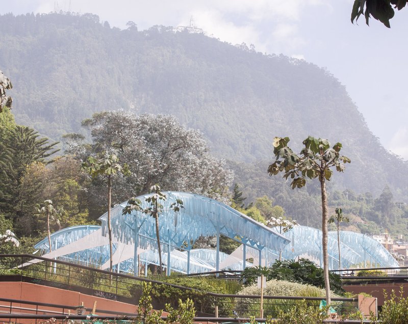 Distant view of the translucent blue ribbed canopy structures rising above trees with a forested hillside beyond