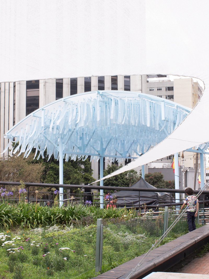 Close view of one curved canopy with vertical blue fins above a planted garden bed and visitor