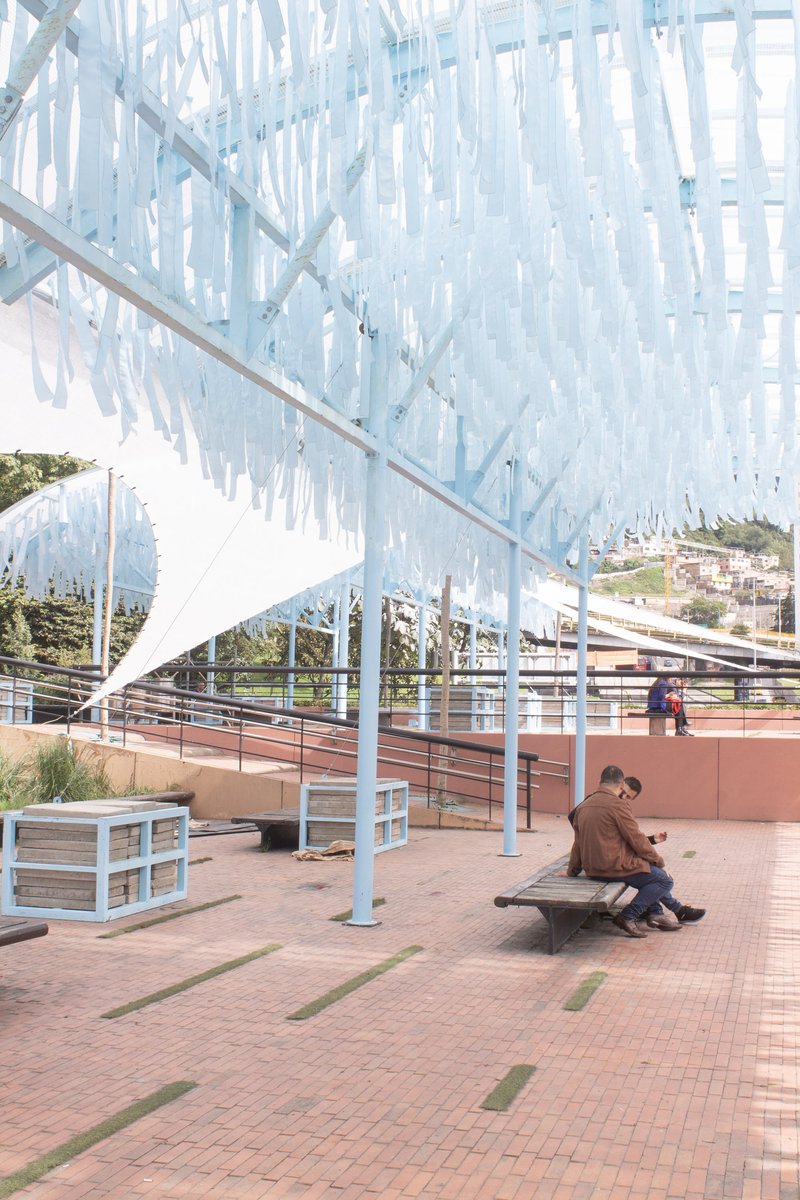 Person seated on a bench under the arched structure with diagonal white columns and blue strips