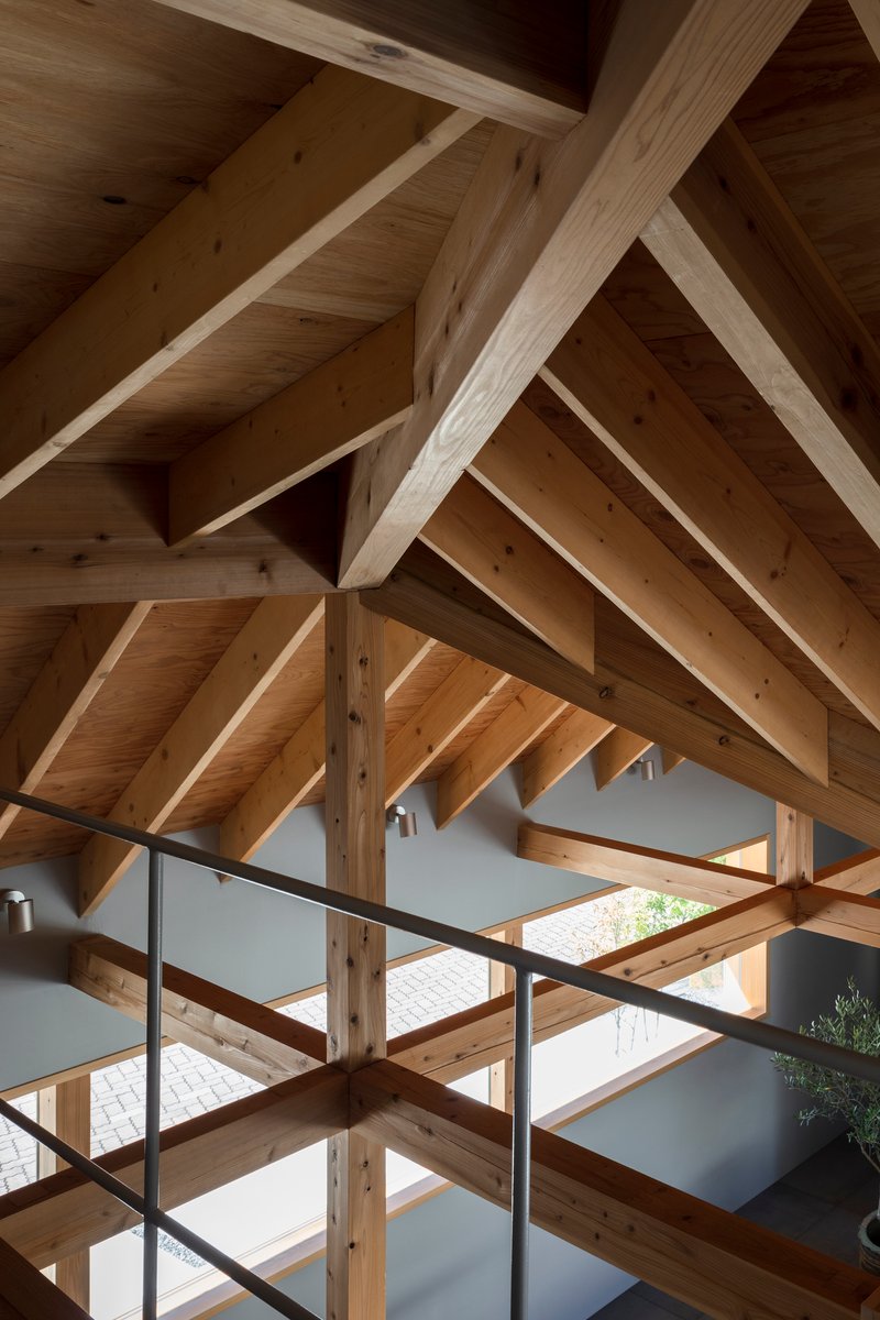 Upward view of the timber roof structure with interlocking beams and rafters above a steel railing