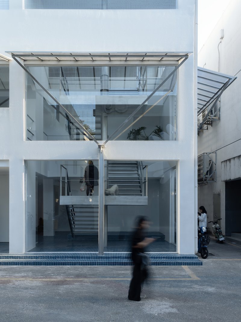 Glass facade showing three-storey interior with central staircase and figures moving in the courtyard at dusk
