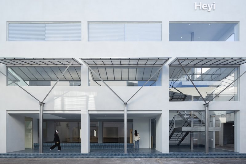 White facade with metal canopy columns and blue tile courtyard floor with two figures passing through