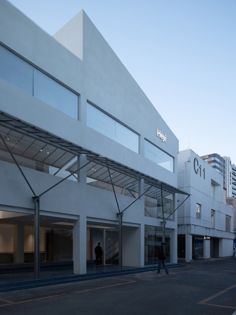 Street facade showing angled metal canopy supported by cables above a ground floor colonnade at dusk