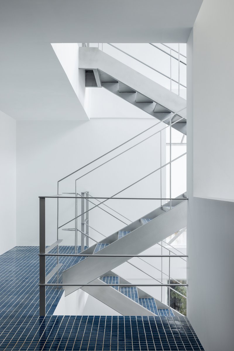 Vertical atrium view showing switchback steel staircases connecting floors with blue mosaic tile landings