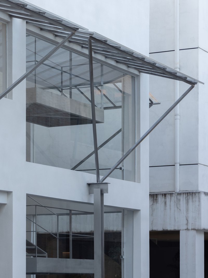 Cantilevered glass box with exposed steel frame and sloped glazed roof projecting from white facade