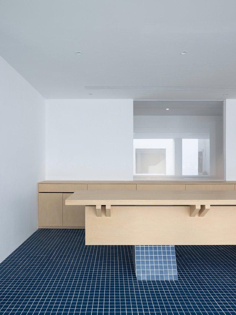 Light wood reception desk with blue mosaic tile floor and white walls under ceiling spotlights