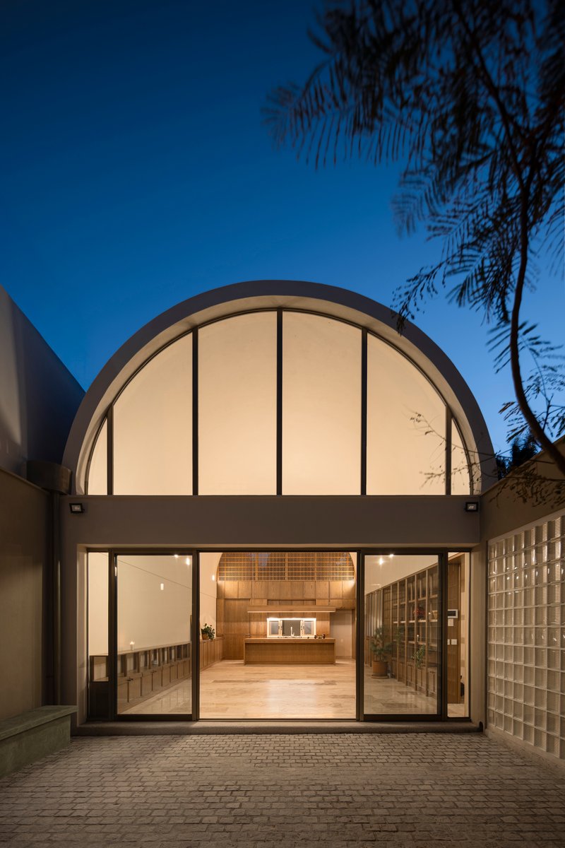 Illuminated arched facade at dusk with sliding glass doors and palm fronds overhead