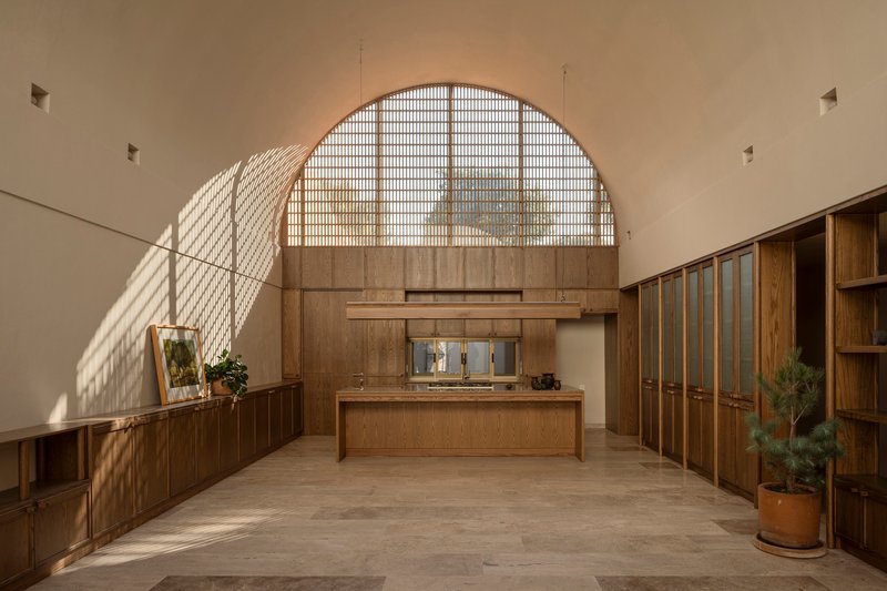 Interior space with arched gridded window casting diagonal shadows across wooden cabinetry and stone flooring