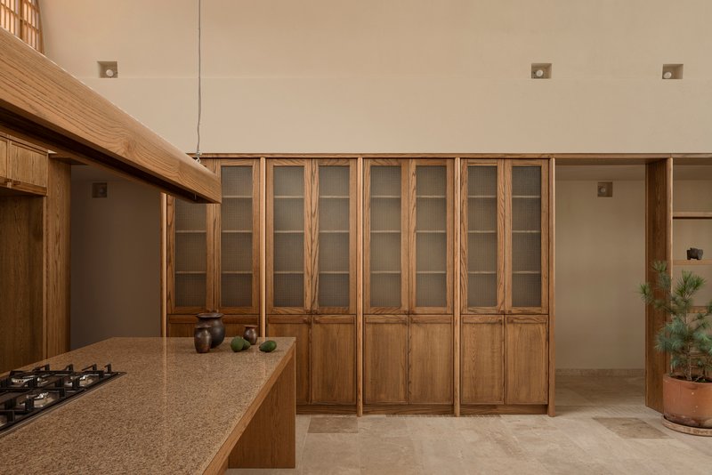 Wooden cabinetry with glass-paneled upper doors flanking a kitchen island with stone countertop