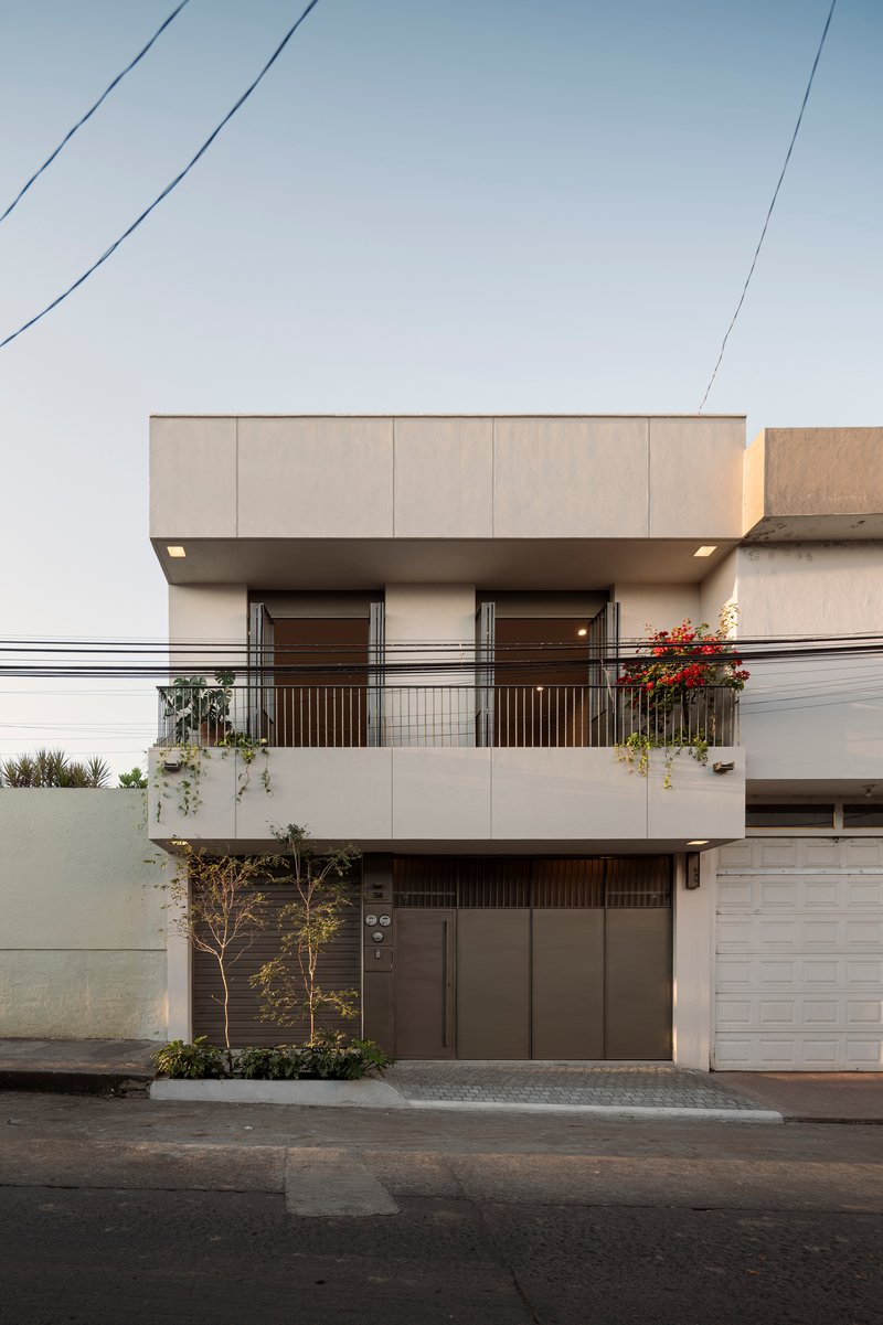 Street facade with cantilevered upper volume, second-floor balcony, and planted terrace with red flowers