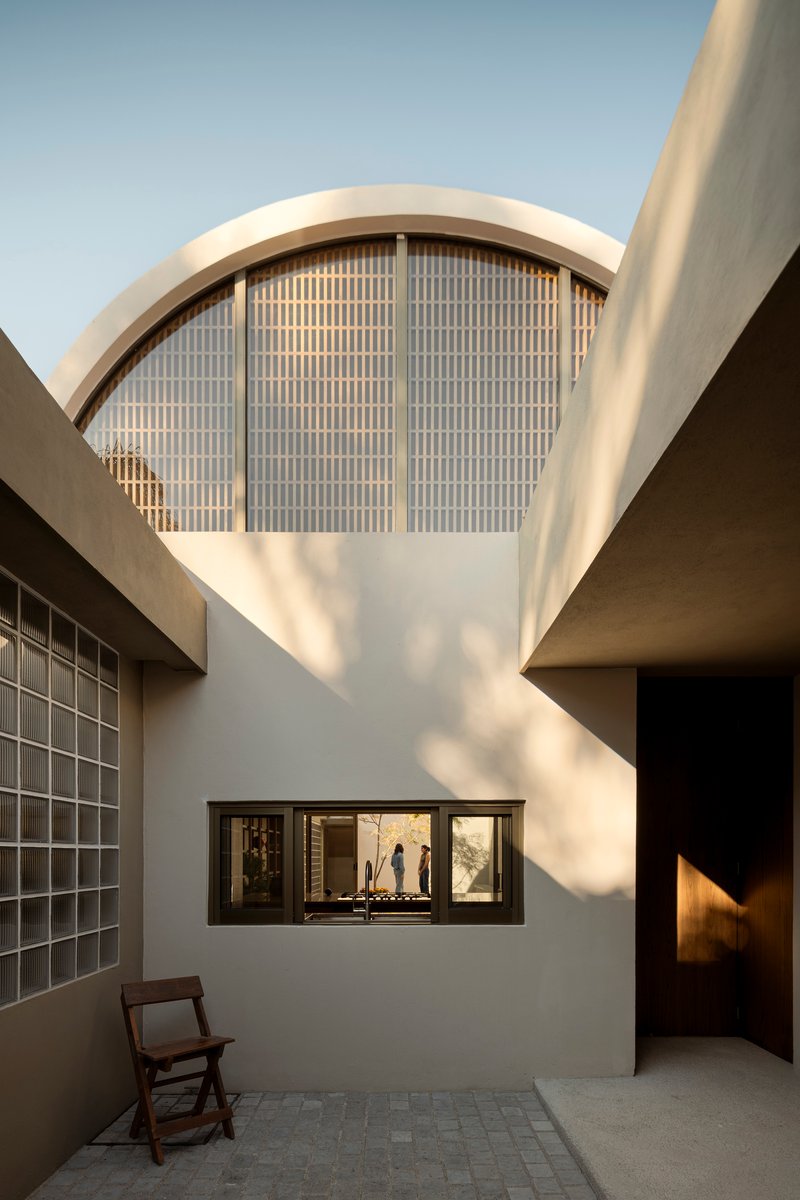Courtyard view of arched window with gridded screen above horizontal openings and wooden folding chair