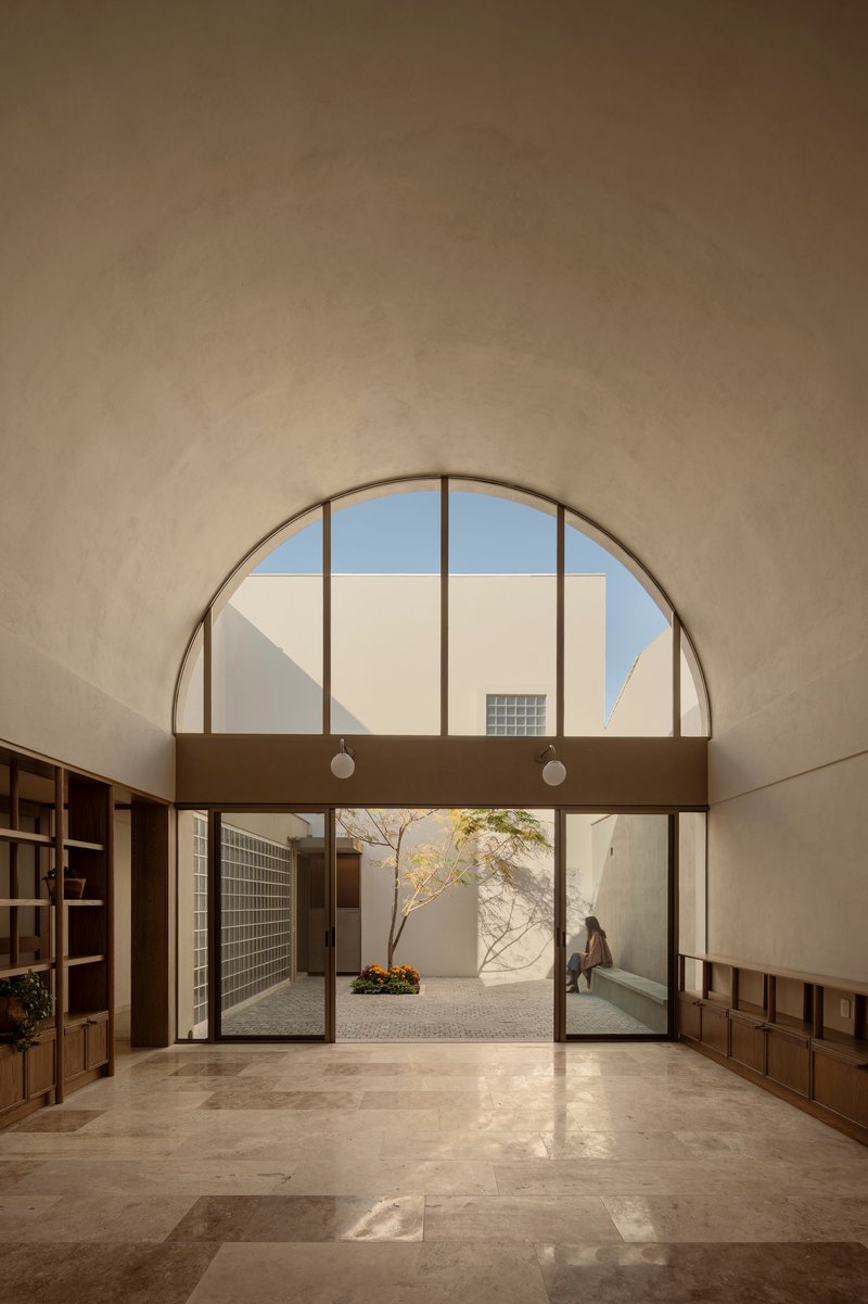 Arched window above glass doors opening to a sunlit courtyard with a figure passing through