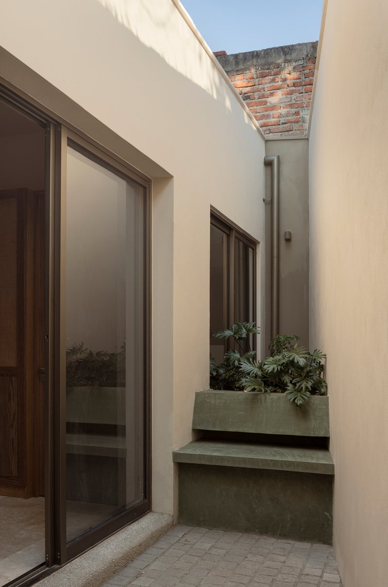 Narrow courtyard with tiered concrete planters and translucent roof panel casting soft light
